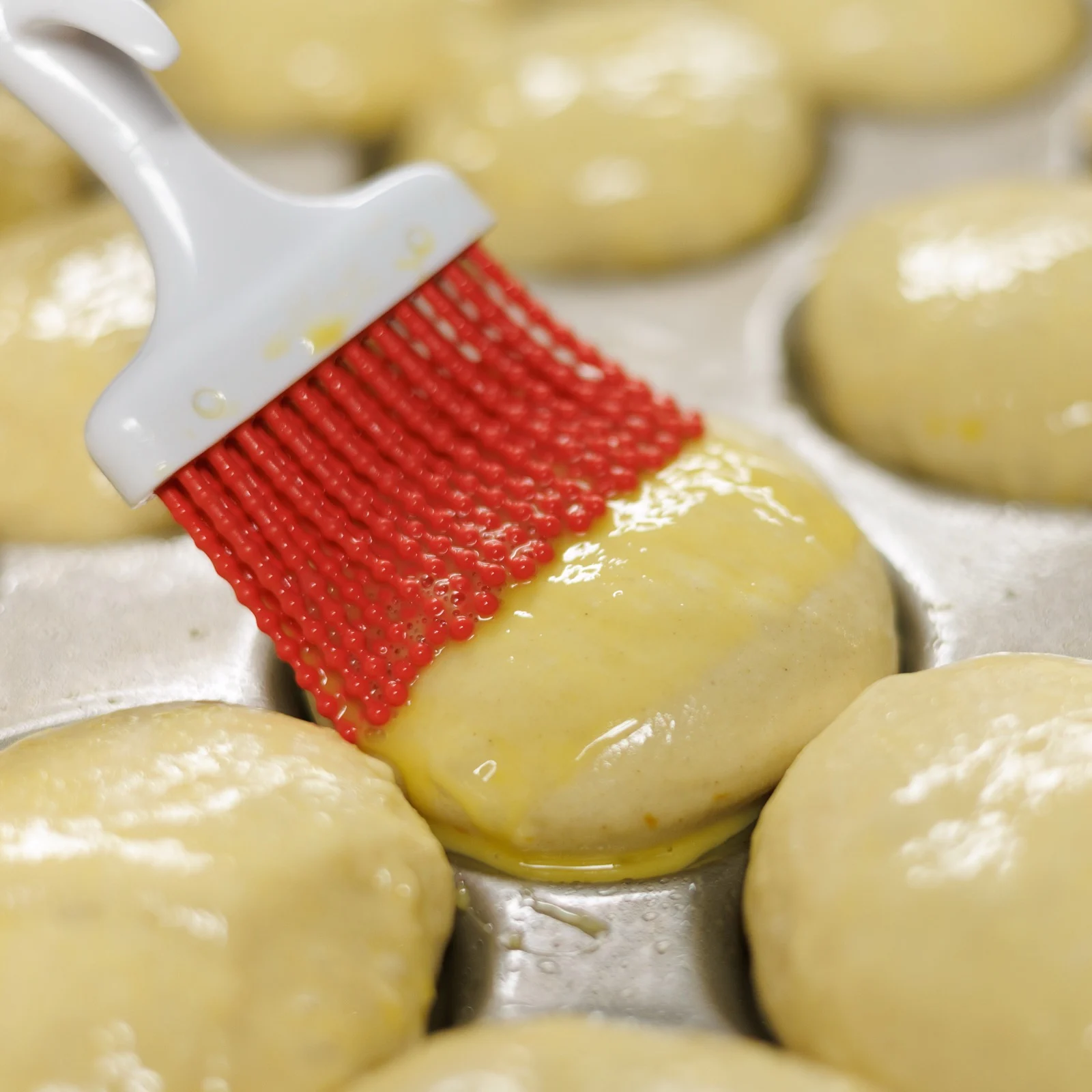 Brushing egg wash on raw buns before baking at Michaels Bakery in Orrville Ohio