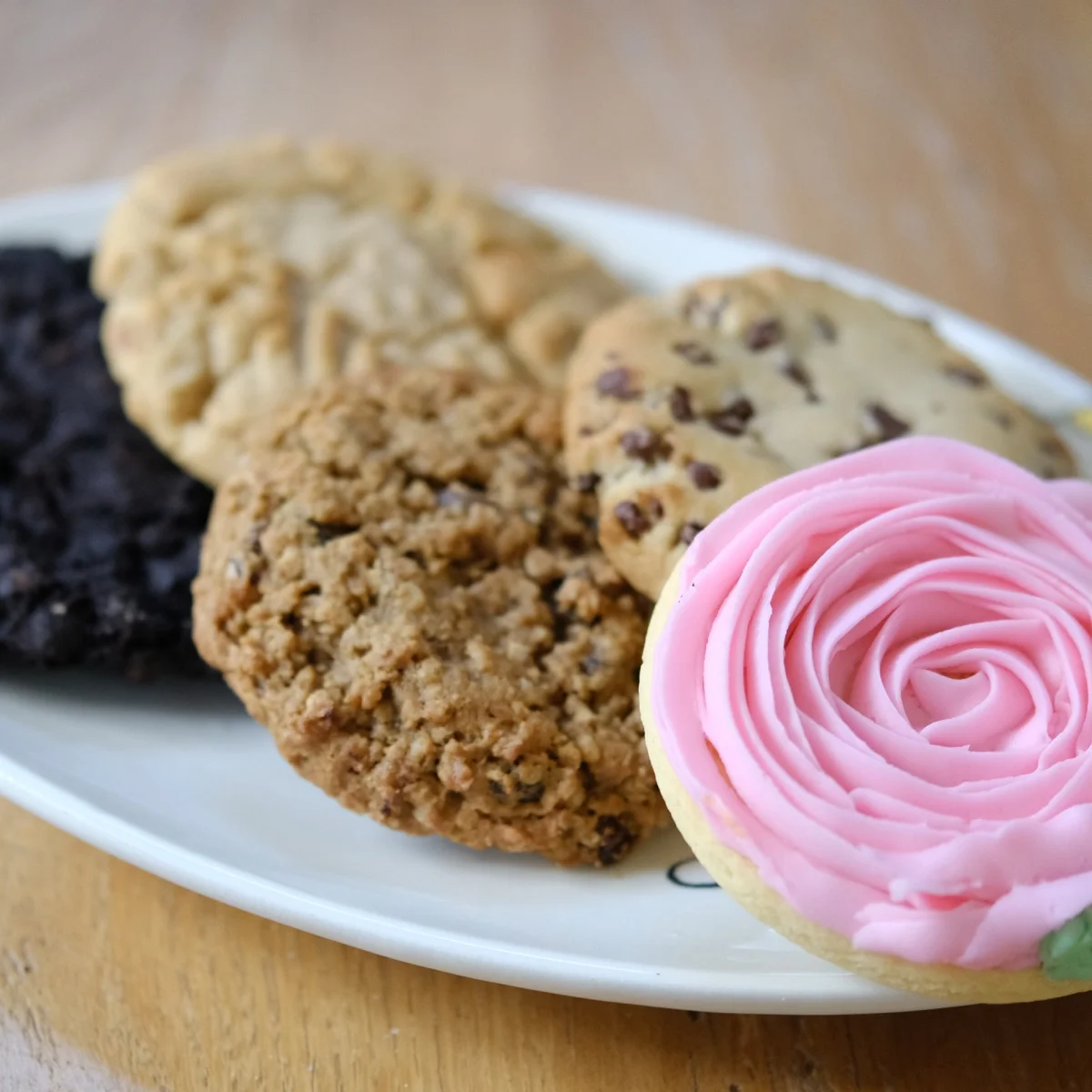 A plate with the new Michaels Bakery cookie lineup: deluxe chocolate, oatmeal raisin, chocolate chip, and an iced rose cutout cookie