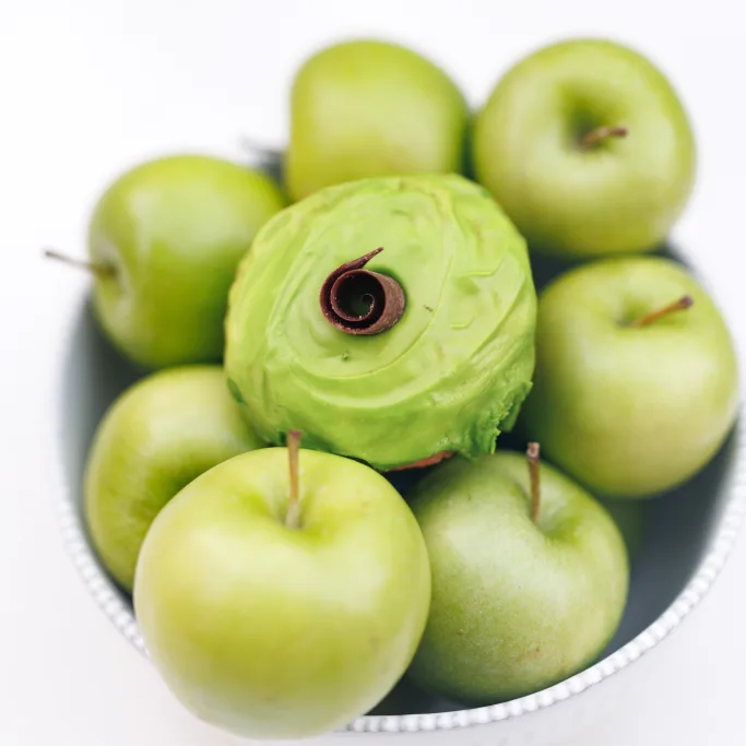 Green apple cake donut with glossy green apple icing in a bowl of fresh green apples, from Michaels Bakery