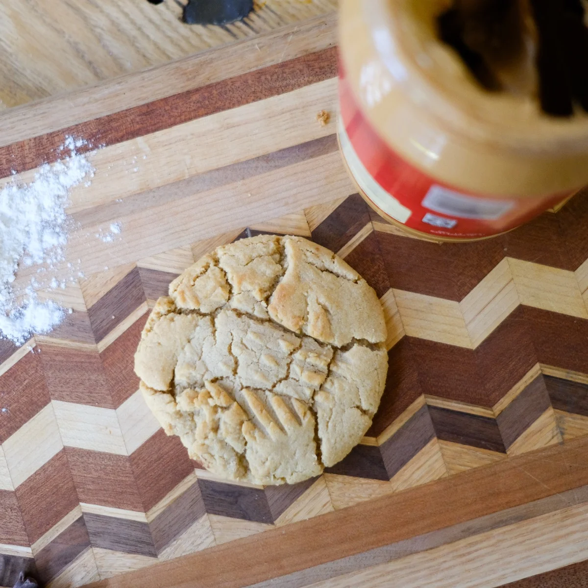 A fresh peanut butter cookie from Michaels Bakery on a wood cutting board with peanut butter jar nearby