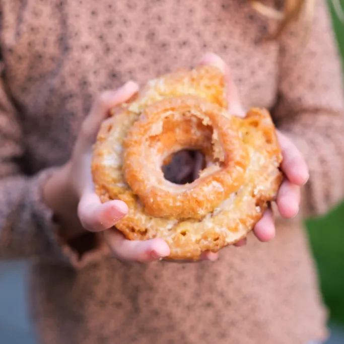 A child holding a glazed pumpkin old-fashioned donut with both hands, from Michaels Bakery in Orrville, Ohio